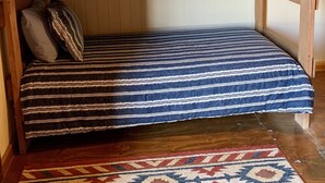 Kerrossänky, jossa on raidallinen vuodevaatteisto, kuvioitu matto ja ikkuna, jossa on ilmastointilaite.
