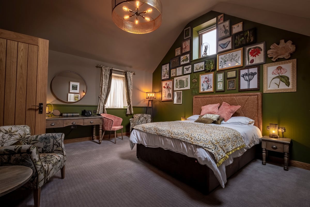 Une chambre à coucher avec un grand lit, un bureau, une chaise, un miroir rond et un mur décoré de tableaux encadrés.