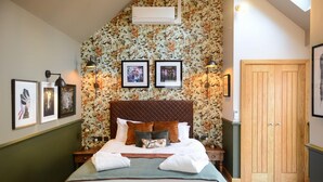 Un dormitorio con cama, cuadros enmarcados, un armario de madera y papel tapiz floral.