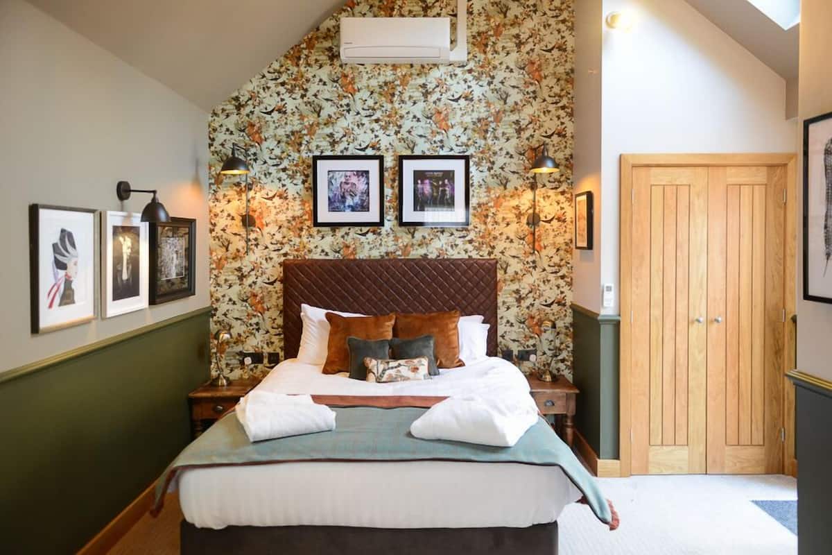 Une chambre à coucher avec un lit, des tableaux encadrés, une armoire en bois et un papier peint à motifs floraux.