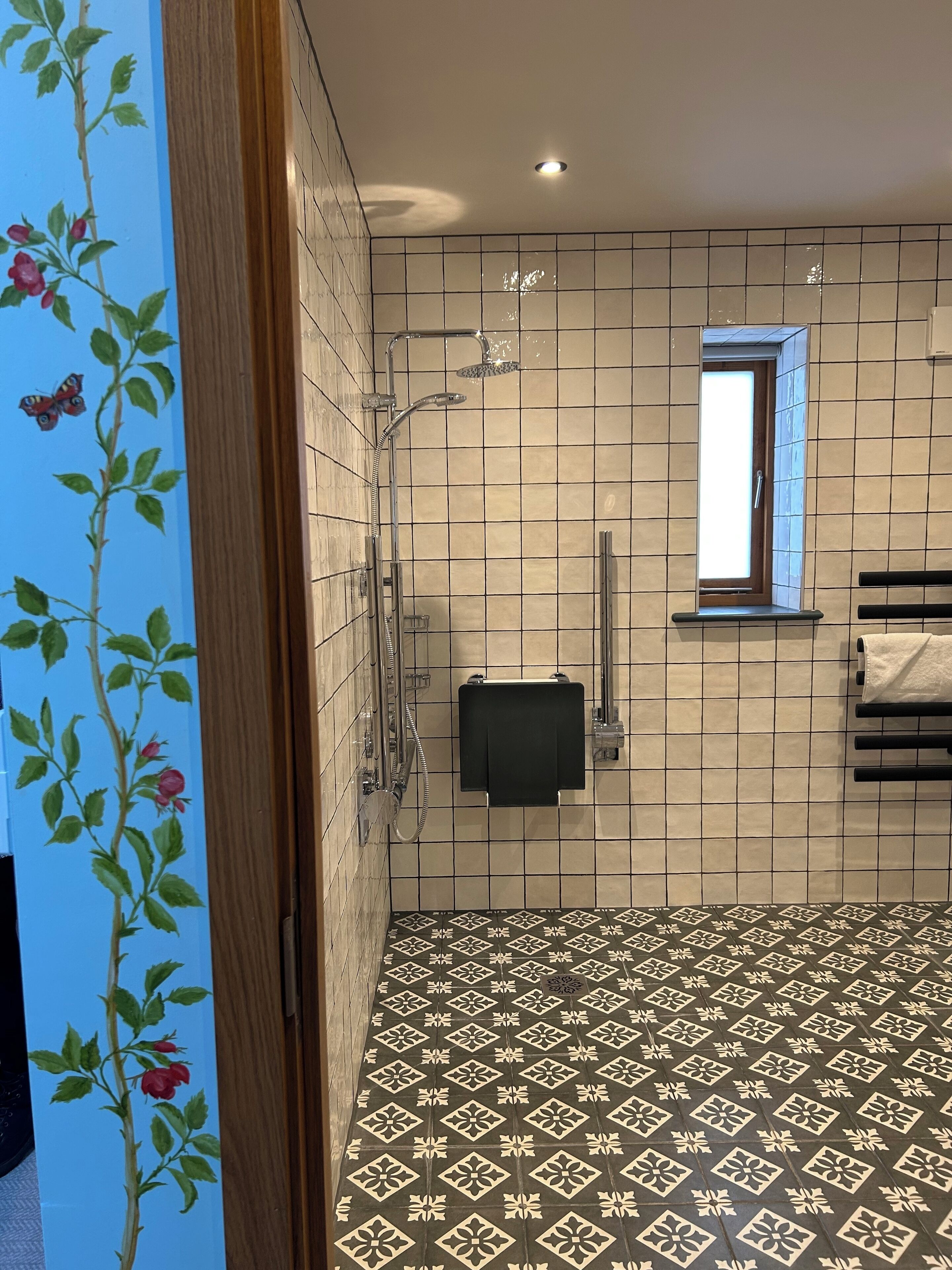 A bathroom with a shower, a small window, and a patterned floor.