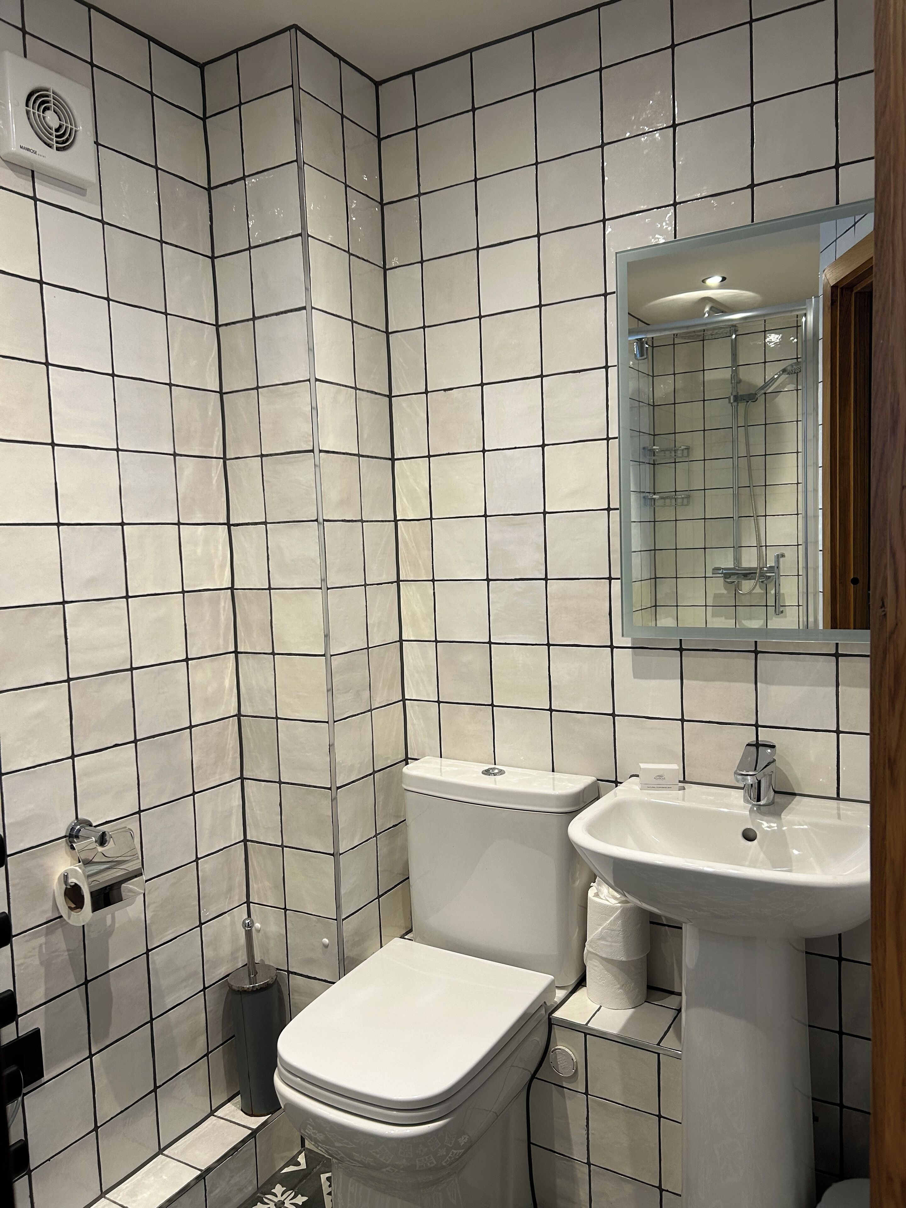 Un baño con paredes de azulejos blancos, un inodoro, un lavabo y un espejo.