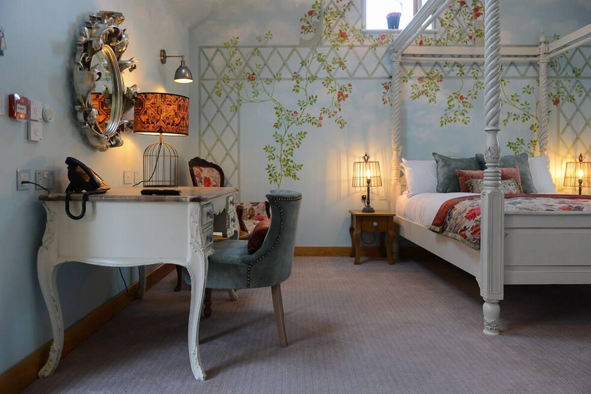 Une chambre à coucher avec un lit à baldaquin, un bureau avec une lampe, une chaise et un miroir décoratif.
