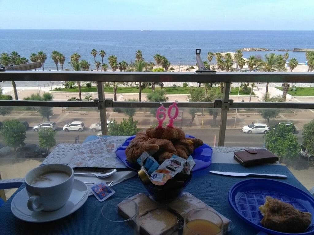 Een balkon met een ontbijttafel, een kop koffie, een schaal gebak en uitzicht op de oceaan en palmbomen.