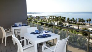 Un balcón con mobiliario blanco de mimbre, una mesa con vajilla azul y vistas al mar y a las palmeras.