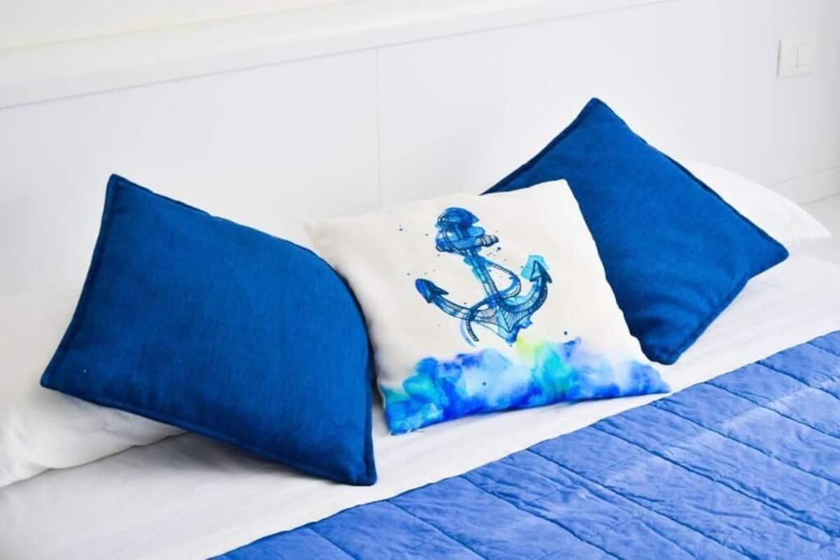 A bed with blue bedding and pillows, one with a nautical anchor design.
