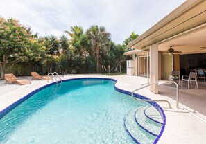 A swimming pool with a blue tiled edge, surrounded by wooden lounge chairs and palm trees. - Casa Del Sol Pool Bungalow | Sleeps 8 | Near Beach (Lake Worth)