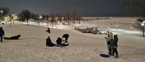 A snowy outdoor area with people sitting and standing, a small shelter, and streetlights.