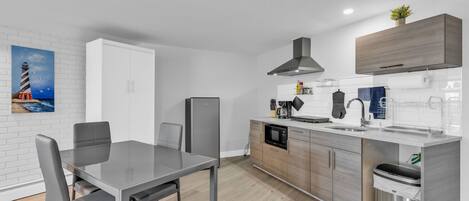 A modern kitchen with a dining area, featuring a stainless steel refrigerator, microwave, and sink.