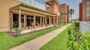 A hotel with a covered outdoor seating area, a pathway, and a well-maintained lawn. - Coral Cave Luxury Condo! Enjoy the beach, pools, BBQs, and bay views.  (South Padre Island)