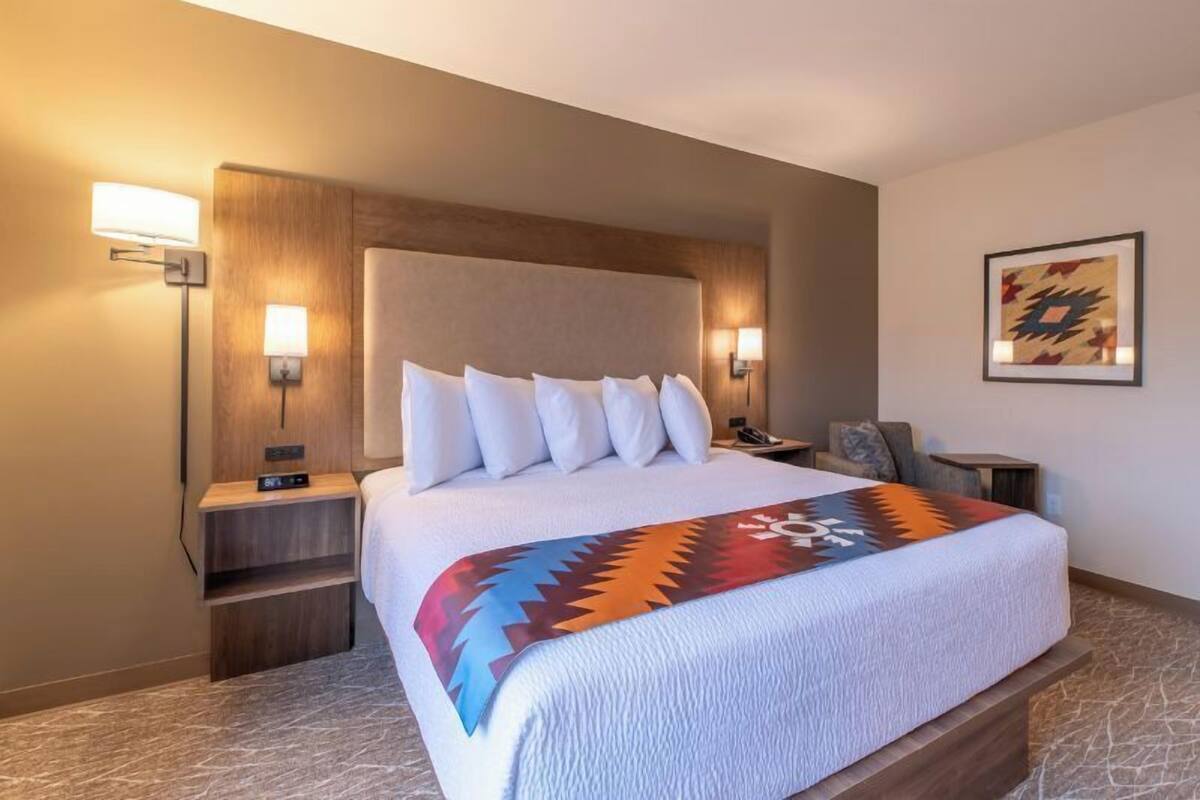 A hotel room with a large bed, two bedside tables, a nightstand, a wall-mounted lamp, and a framed picture on the wall.