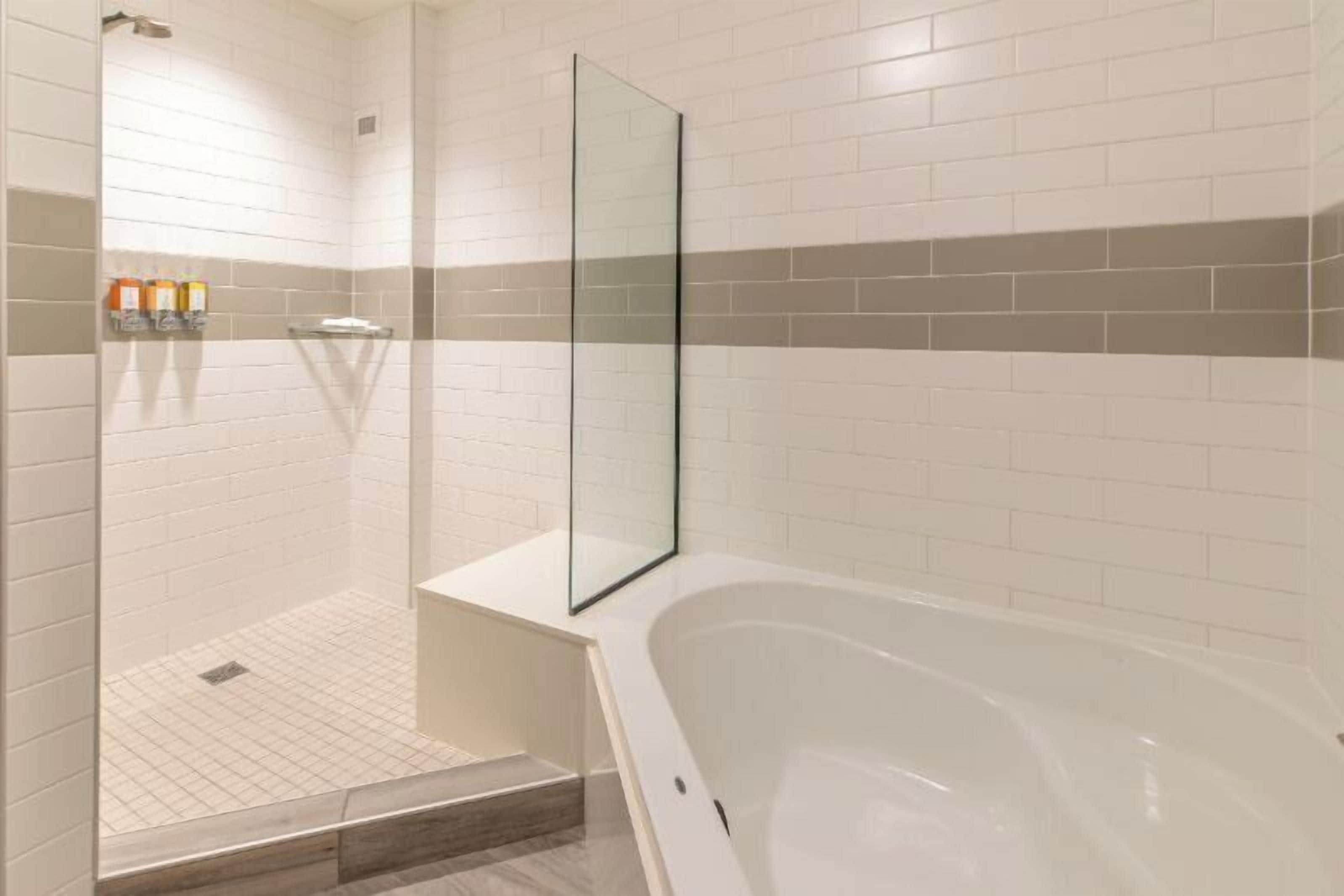 A modern bathroom with a glass shower enclosure, a white bathtub, and a tiled floor.