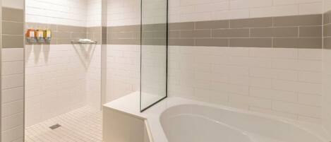 Un baño moderno con mampara de vidrio, bañera blanca y suelo de baldosas.