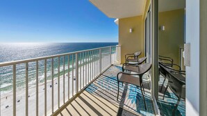A balcony with a view of the ocean, a chair, and a small table.
