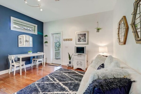 Un salon avec un mur bleu, un canapé blanc, une table à manger avec des chaises, un téléviseur posé sur un meuble blanc et des œuvres d’art décoratives accrochées au mur.