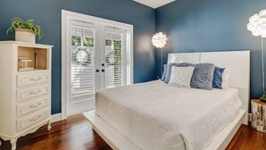 Ein Schlafzimmer mit einem weißen Bett, einer weißen Kommode und einer blauen Wand.