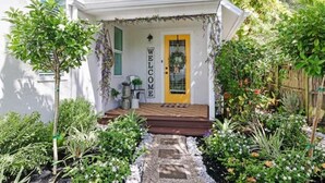 Ein Haus mit gelber Tür, einem Willkommensschild und einem Garten mit verschiedenen Pflanzen sowie einem Weg, der zur Tür führt.