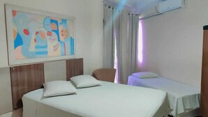 Une chambre d’hôtel avec un grand tableau abstrait au mur, deux lits avec du linge de lit blanc, une tête de lit en bois et une chaise.
