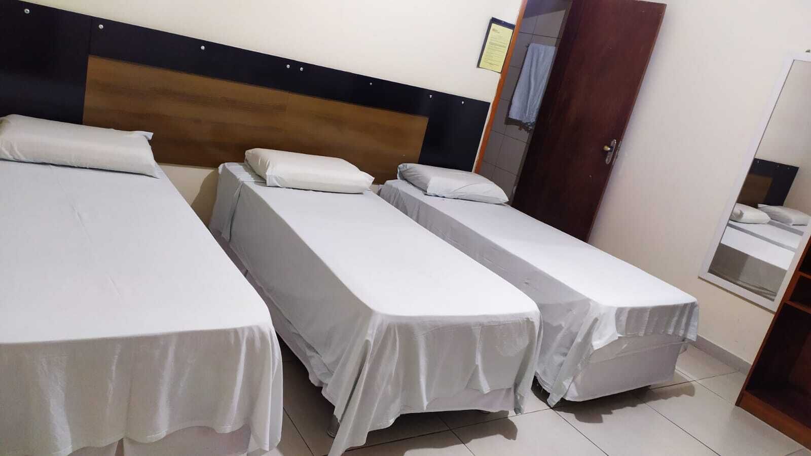 Een hotelkamer met drie eenpersoonsbedden, een houten hoofdbord, een kleine badkamer en een houten garderobe.