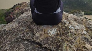 Une personne assise sur un rocher, avec une vue sur une rivière et des montagnes en arrière-plan.