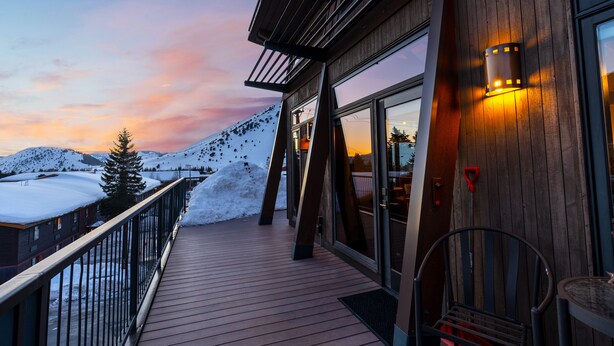 A wooden deck with a glass door leading to a room, a chair, and a snow-covered mountain in the background. - Pearl Penthouse by Jackson Vacations (Jackson)