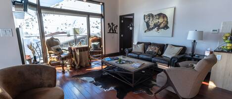 A spacious living room with a large window, a leather sofa, a coffee table, and a cowhide rug.