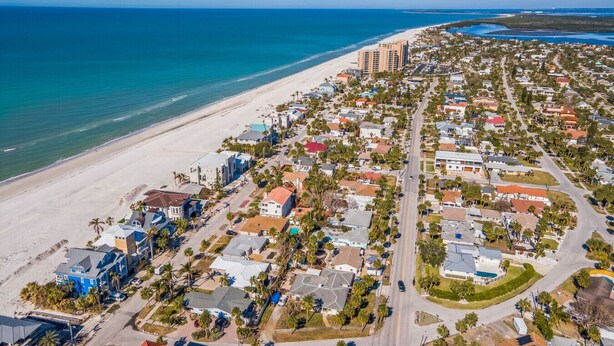 An aerial view of a coastal town with a beach, residential buildings, and a few high-rise hotels.