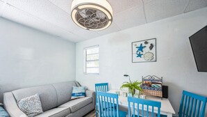 A cozy room with a gray sofa, blue chairs, a small table, and a ceiling fan.