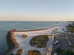 Une zone de plage côtière avec un parking, une route et une jetée qui s’avance dans l’eau.