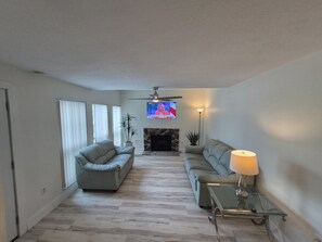 A living room with a fireplace, two sofas, a TV, and a ceiling fan.