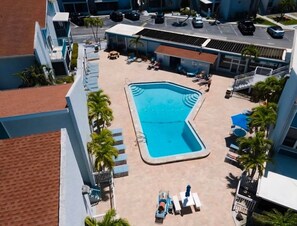 An aerial view of a hotel with a central swimming pool, sun loungers, and palm trees.