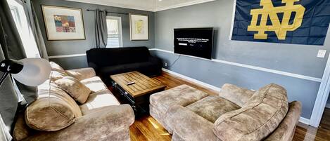 Ein Wohnzimmer mit einem schwarzen Sofa, zwei beigen Couches, einem Holztisch, einem Deckenventilator und einem Fernseher, der eine Nachricht zeigt.