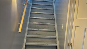 Una escalera con barandilla, una lámpara en la pared y una puerta al final.