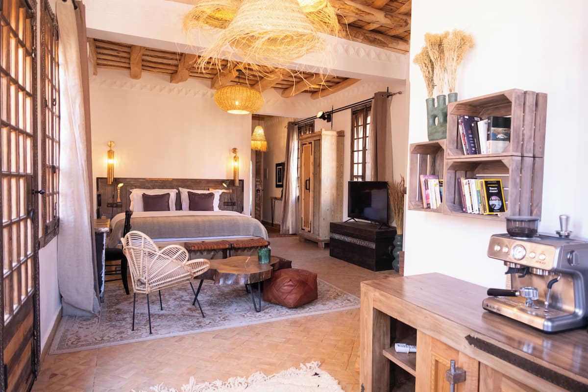 A cozy bedroom with a bed, a coffee machine, a bookshelf, and a television.