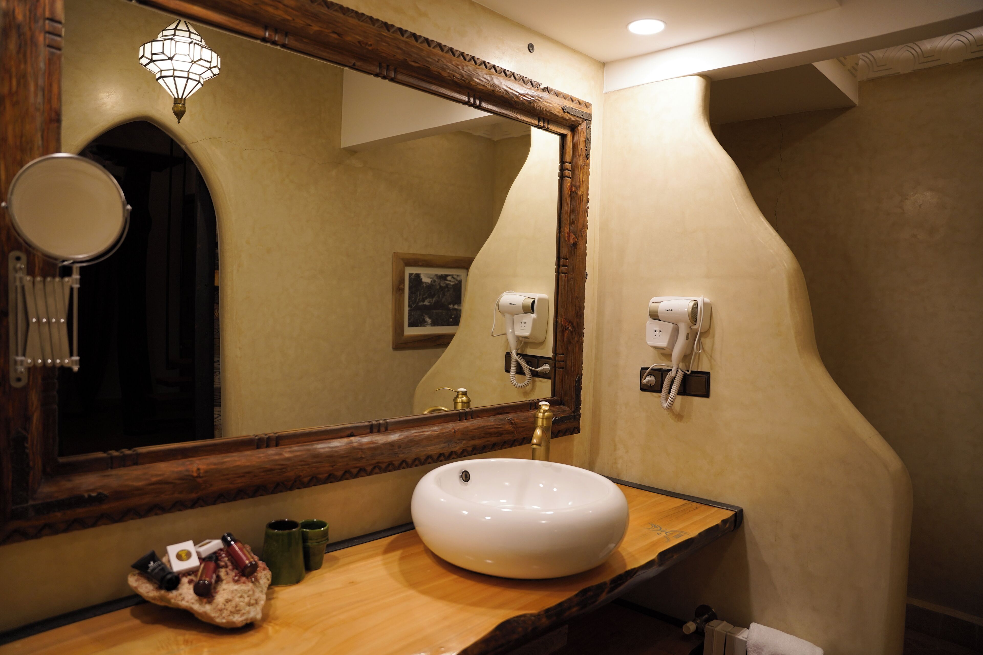 A bathroom with a round mirror, a white sink, a wooden vanity, a towel rack, and a hairdryer.