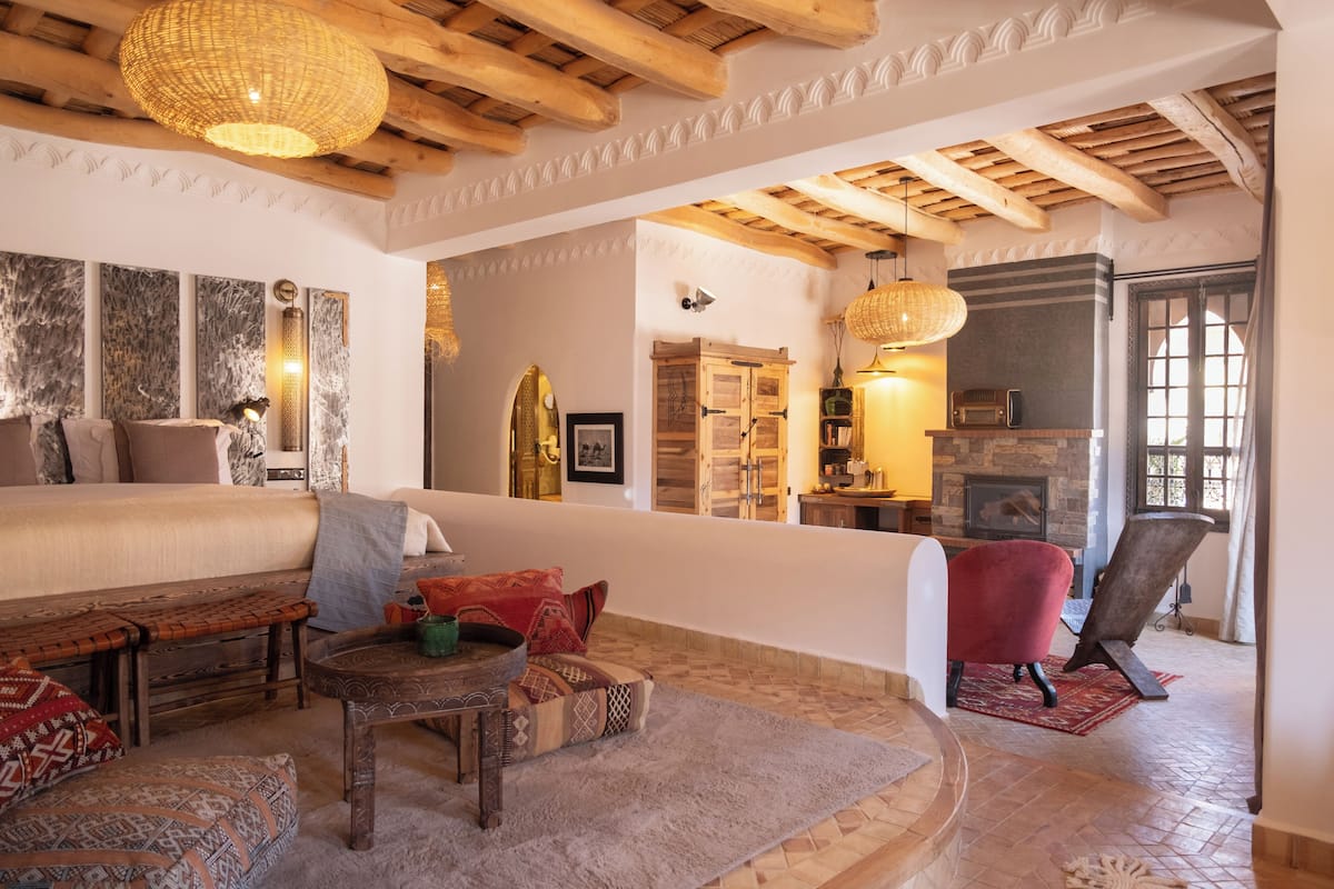 A spacious living area with a high ceiling, wooden beams, a fireplace, and a cozy seating arrangement.