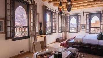 A room with a bed, a chair, a table, and large windows with views of rocky terrain.