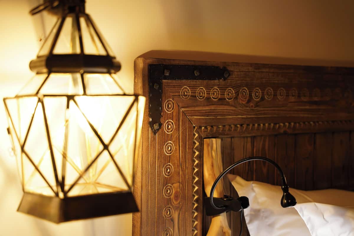 A wooden bed frame with a headboard, a hanging lantern, and a bedside lamp.