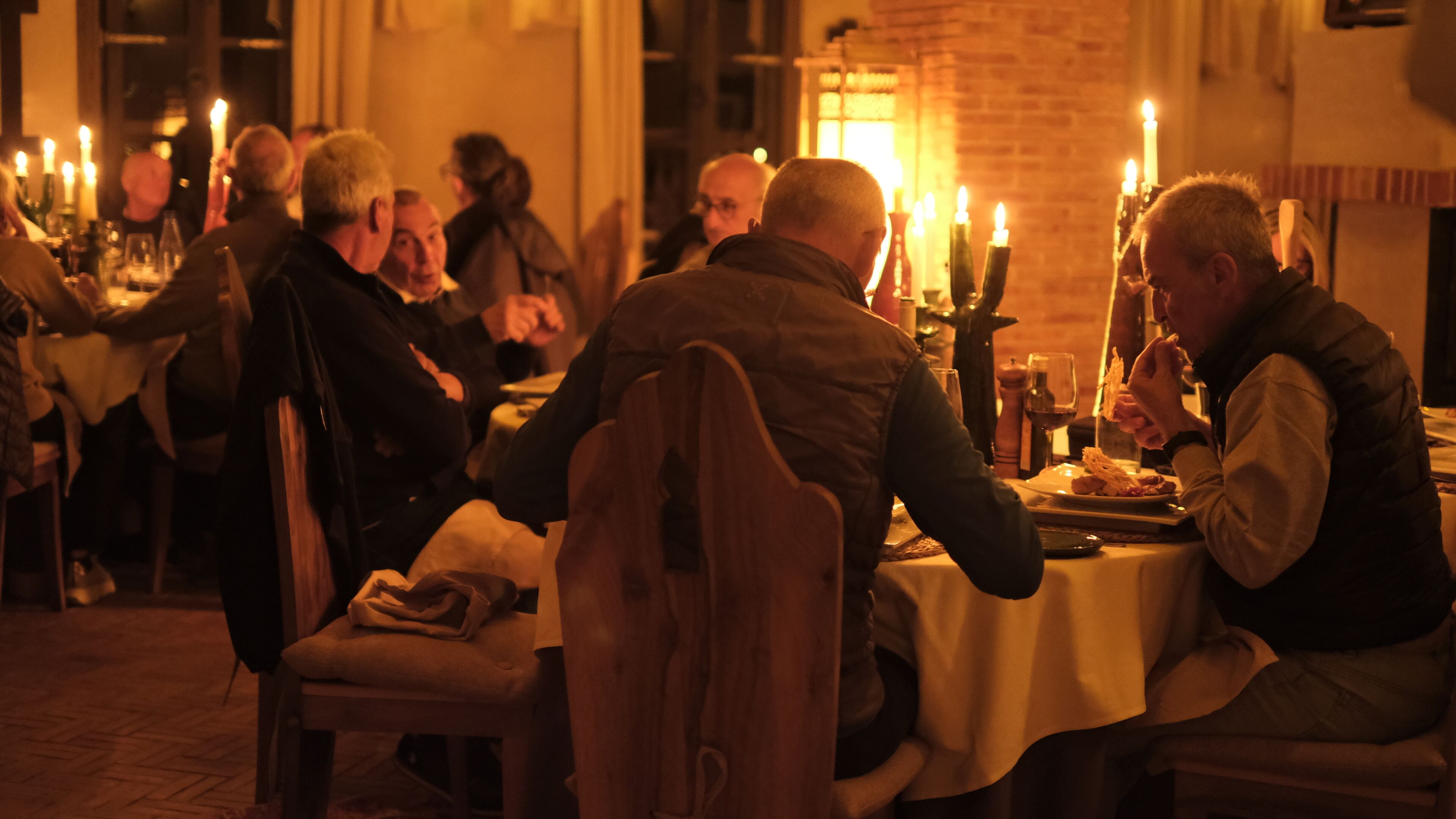 Un groupe de personnes est réuni autour d’une table, éclairée à la bougie, dans un cadre intérieur chaleureux.