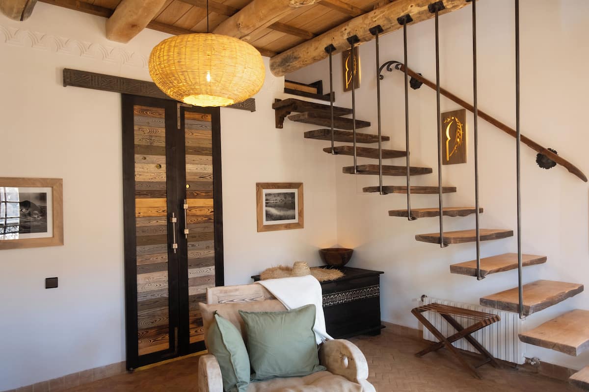 A wooden staircase with a woven light fixture above, a cushioned chair, and a radiator below.