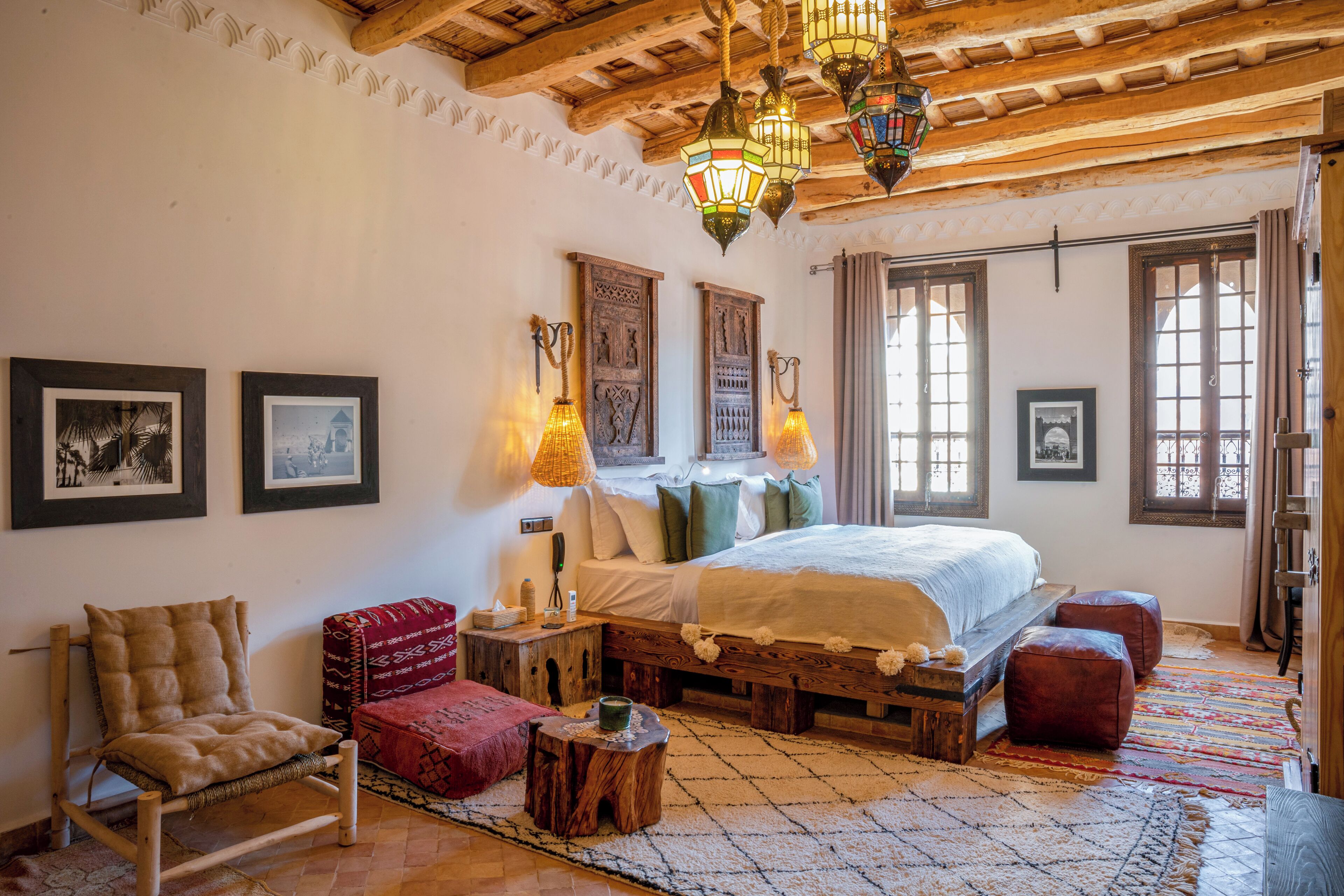 Een slaapkamer met een groot bed, houten balken, een houten bankje, een stoel en een vloerkleed.
