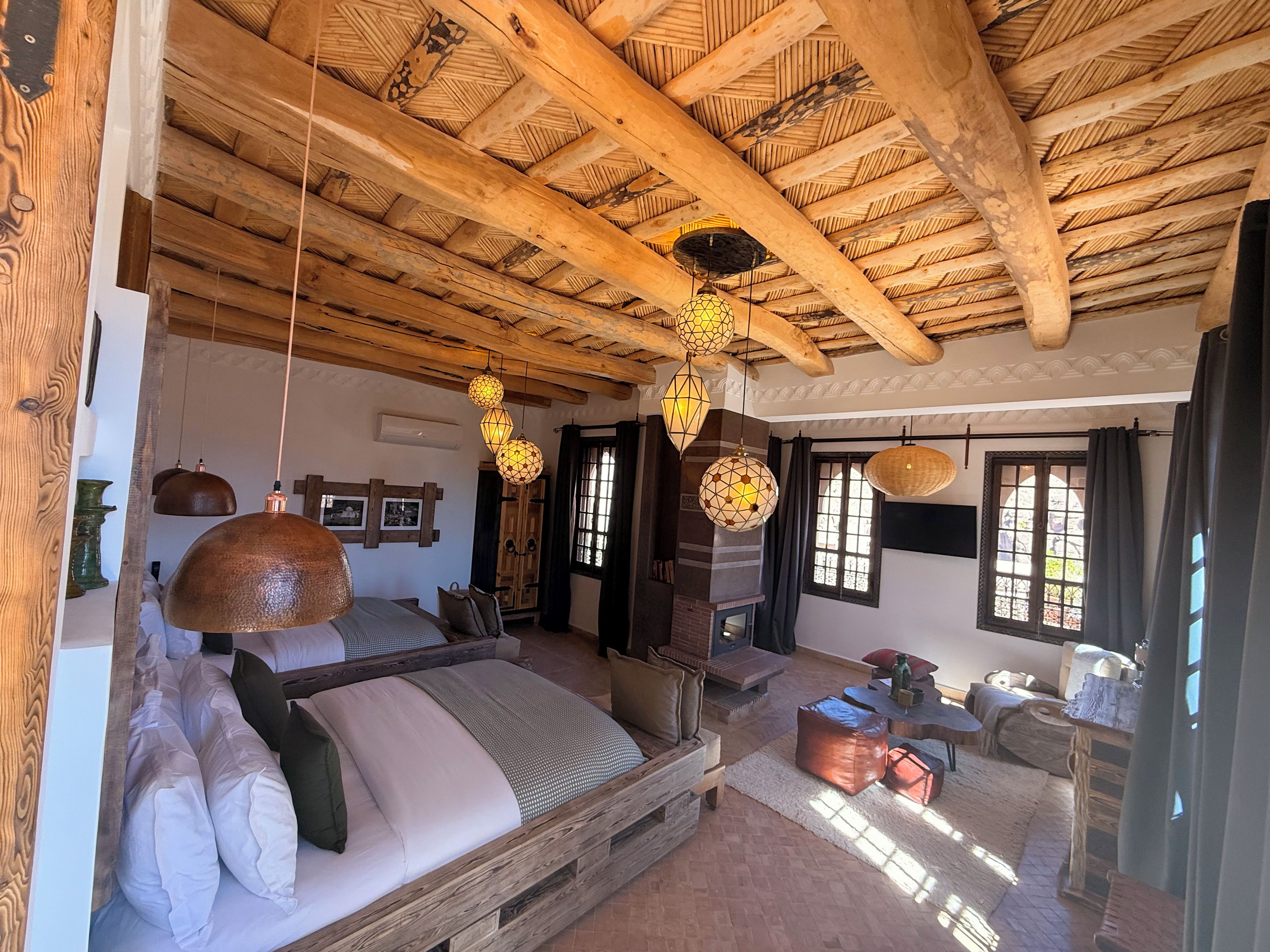 A rustic bedroom with a wooden bed, hanging lamps, and a brick fireplace.