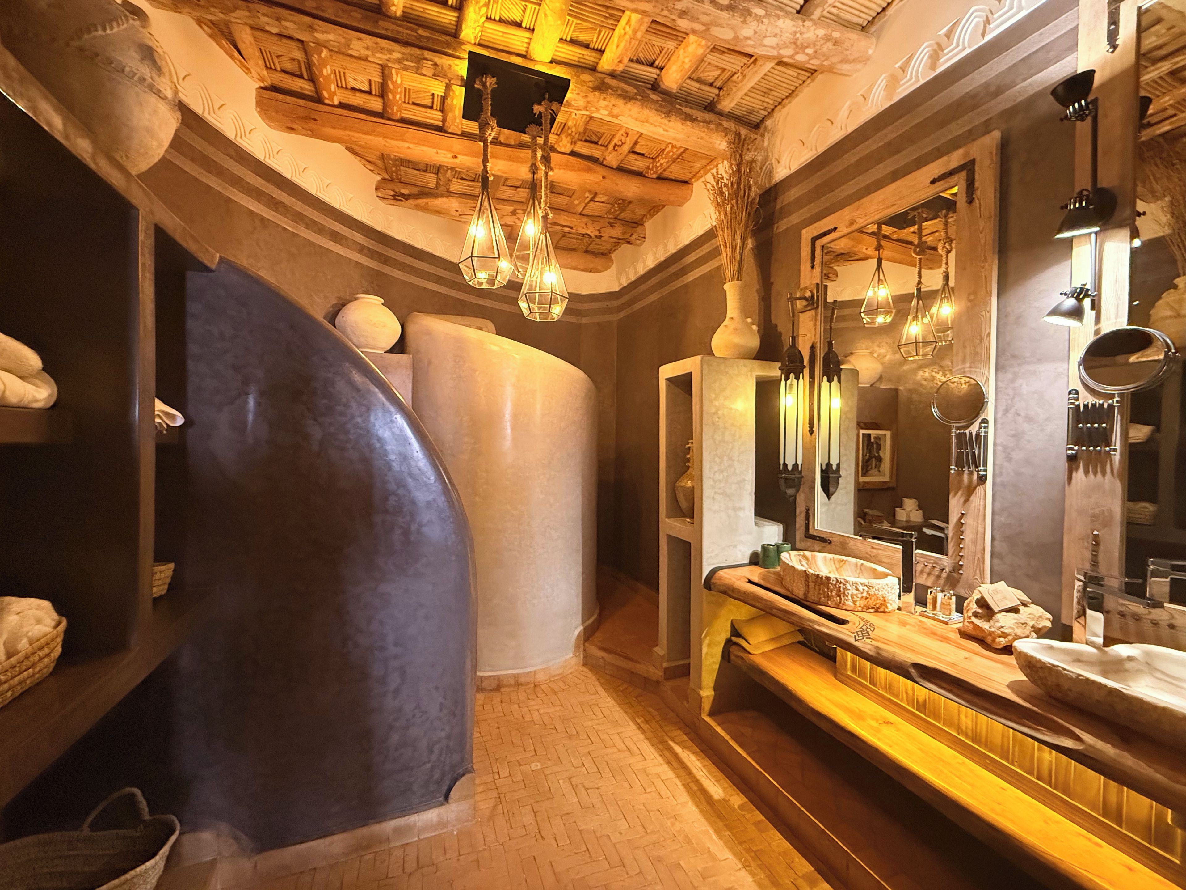 A bathroom with a curved wall, a vanity with a mirror, and a wooden bench.