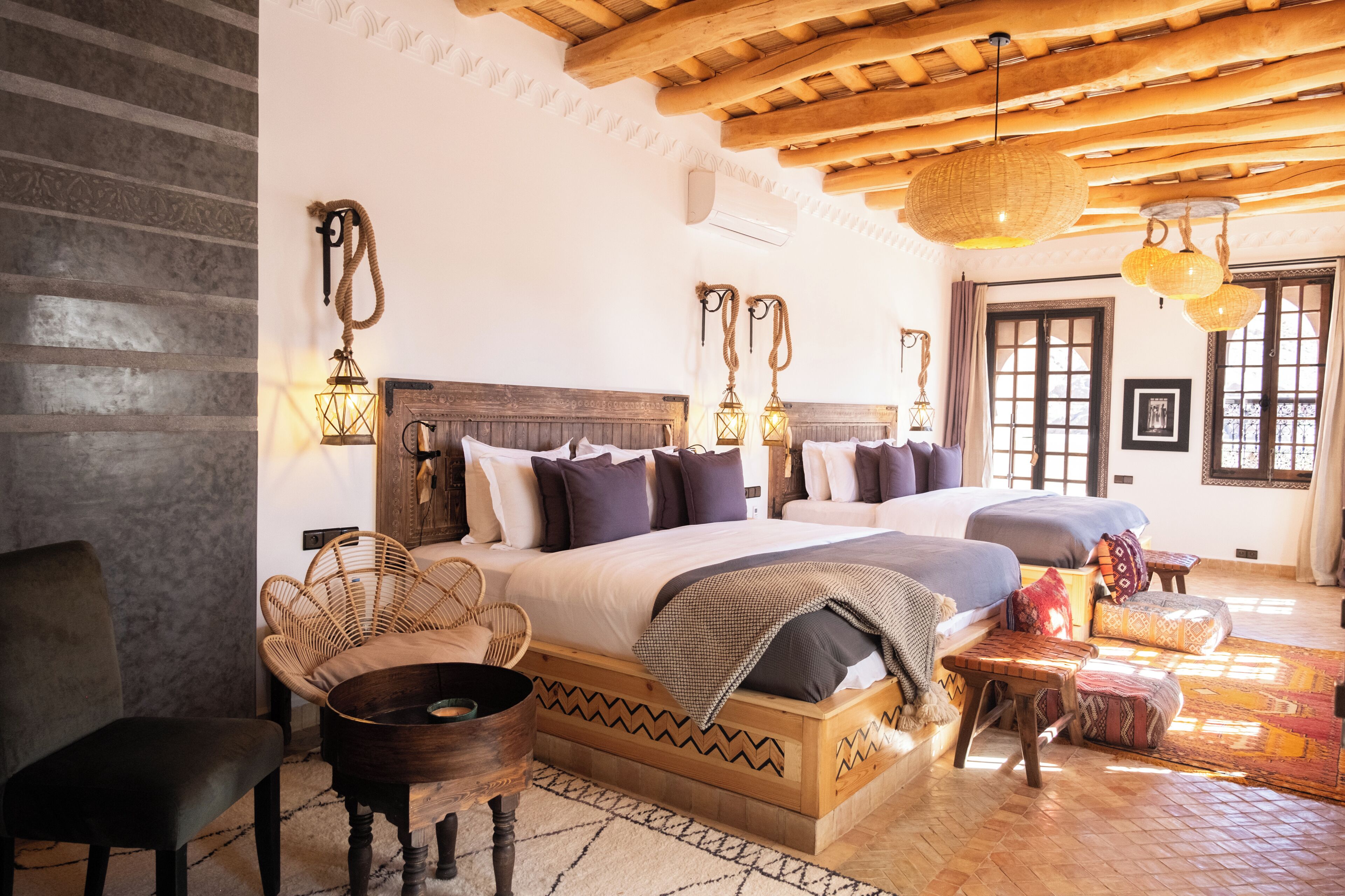 Un dormitorio amplio con una cama grande, dos camas más pequeñas, cabecero de madera, sillas de mimbre y suelo de madera rústica.