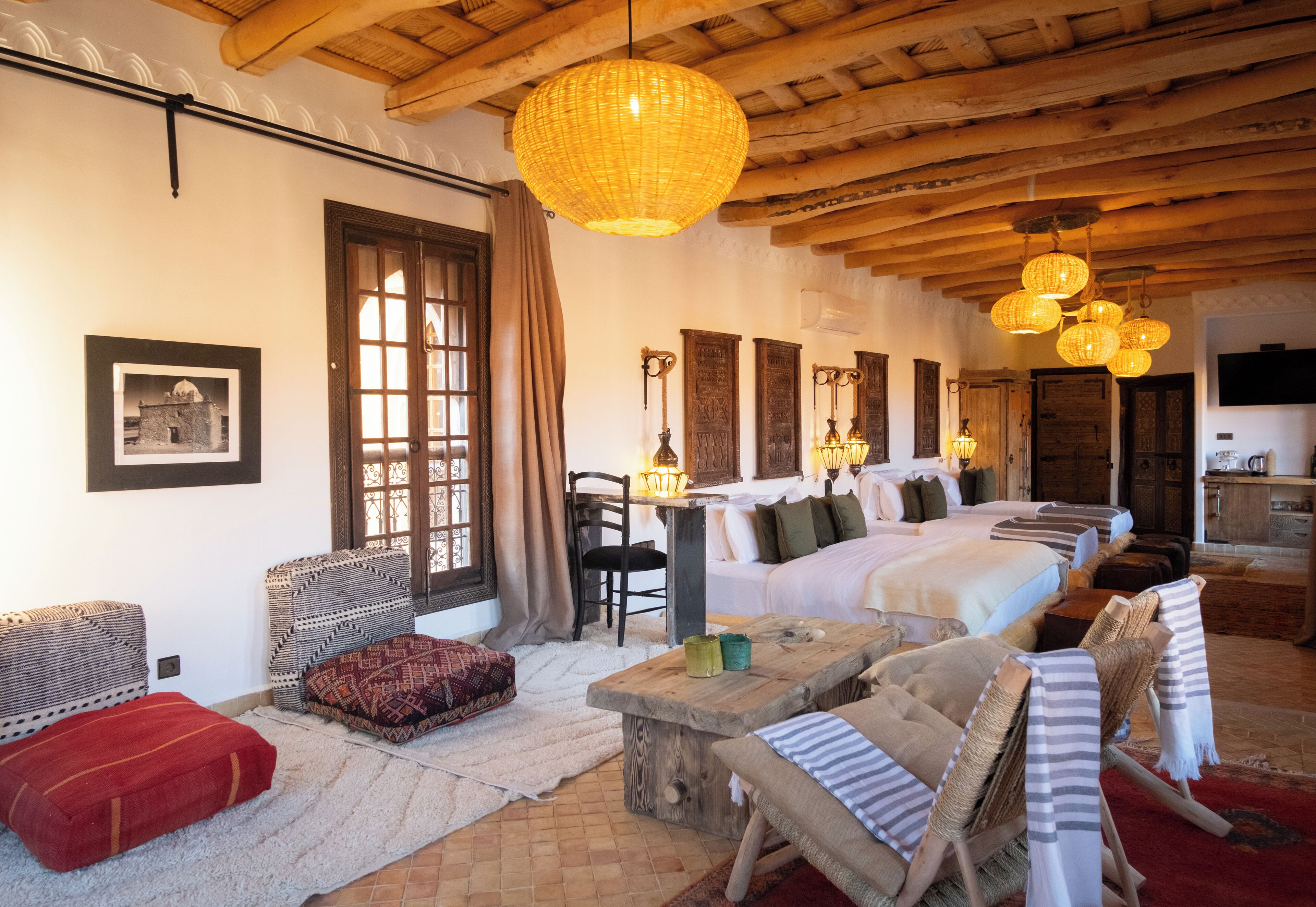 Una habitación acogedora con una cama grande, una mesa de madera y una silla de mimbre. Hay varias ventanas con cortinas, una chimenea y un televisor en la pared.
