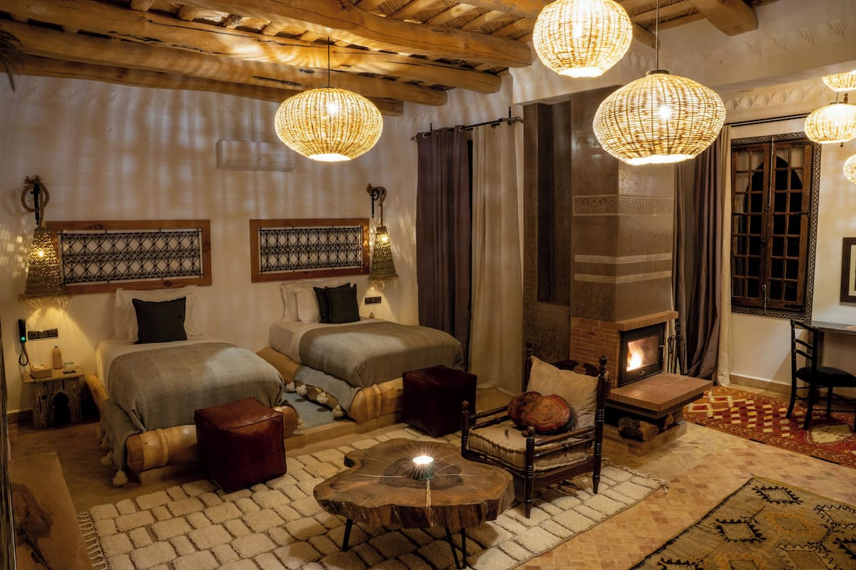 A cozy room with two beds, a fireplace, and wicker chandeliers.