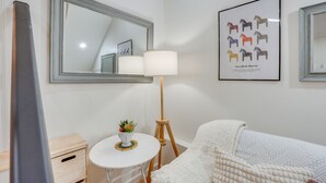 Un dormitorio ordenado con un espejo grande, un cuadro enmarcado de caballos suecos, una lámpara de noche, una mesita con una planta y una cama acogedora con un edredón estampado.