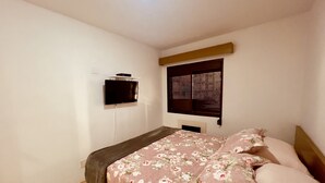 A bedroom with a bed, a television mounted on the wall, and a window with blinds. - Apartamento Alameda Jaú, Jardins, SP (Jardim Paulista São Paulo)