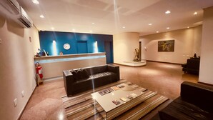 A modern lobby with a reception desk, a black leather sofa, a coffee table with magazines, and a painting on the wall. - Apartamento Alameda Jaú, Jardins, SP (Jardim Paulista São Paulo)