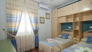 A bedroom with two beds, a wooden wardrobe, and a desk.